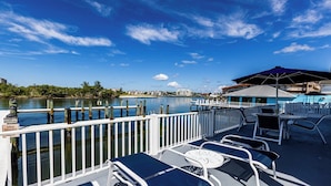A waterfront deck with lounge chairs, a table, and a view of the water and buildings.