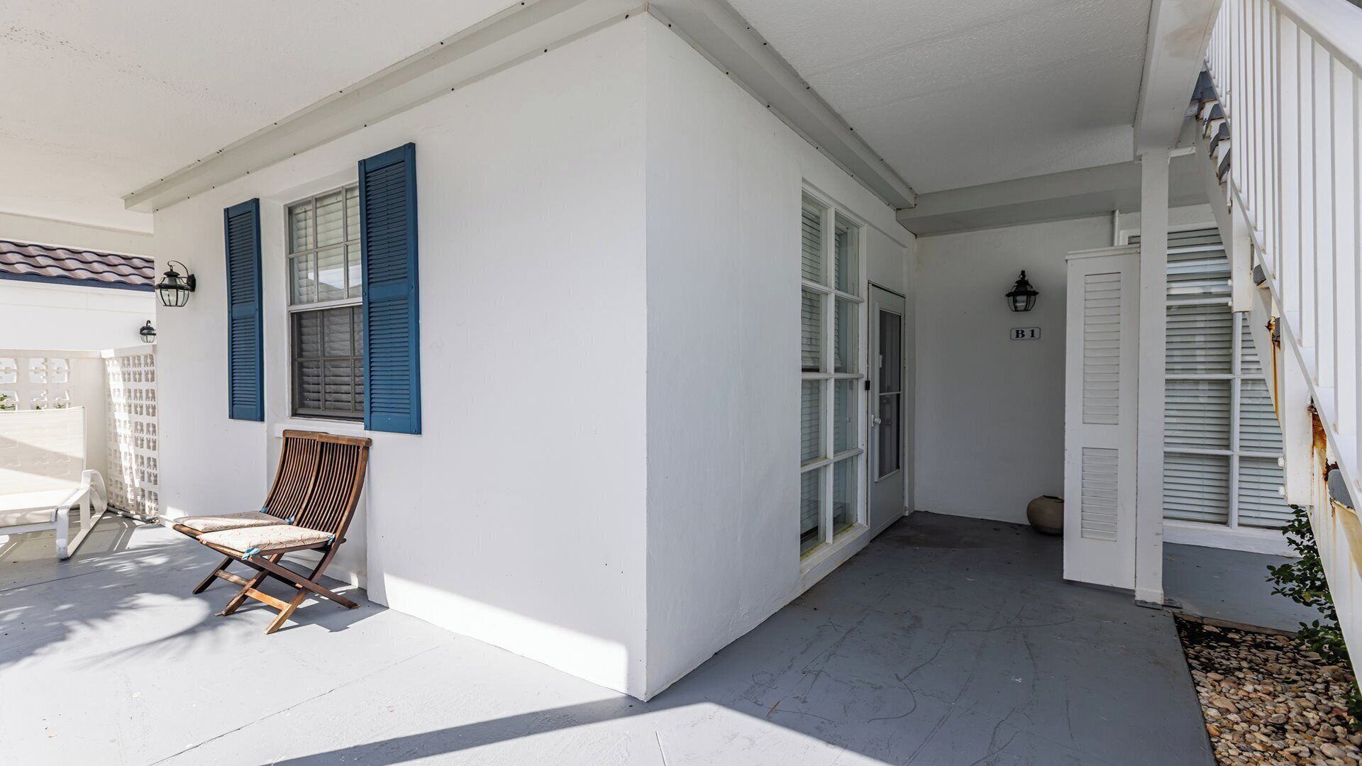 A white building with blue shutters, a wooden chair, and a door marked B1.