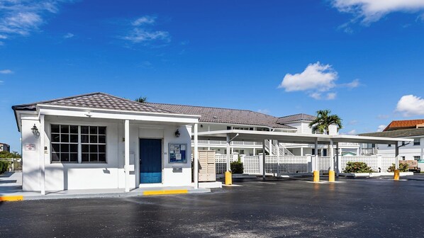 A white building with a blue door, a covered outdoor area, and a parking lot.