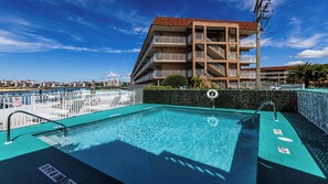 A swimming pool with a 3ft 6in depth sign, surrounded by a white fence, and a building with balconies in the background.