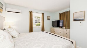 Ein Schlafzimmer mit einem Bett, einem Fernseher, einem Schminktisch und einem Fenster mit Vorhängen.