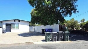 Un edificio con puerta de garaje, área cercada y varios contenedores de basura.