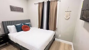Un dormitorio con cama, almohadas, una mesita de noche y un adorno macramé en la pared.