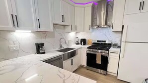 Una cocina moderna con armarios blancos, un lavamanos de acero inoxidable, una estufa a gas y un horno empotrado.