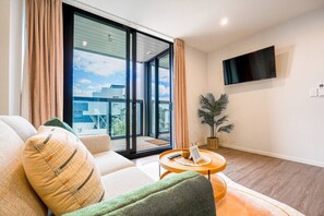 A modern living room with a sofa, a small round table, a potted plant, and a TV mounted on the wall.