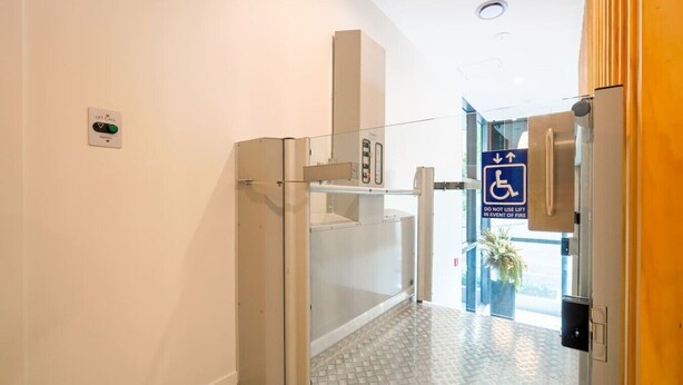 A hotel entrance with a lift call button, a wheelchair access sign, and a glass door.