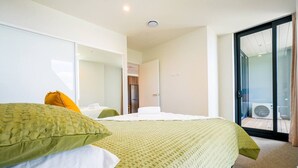 A hotel room with a bed, a chair, a door, and a view of the outside.