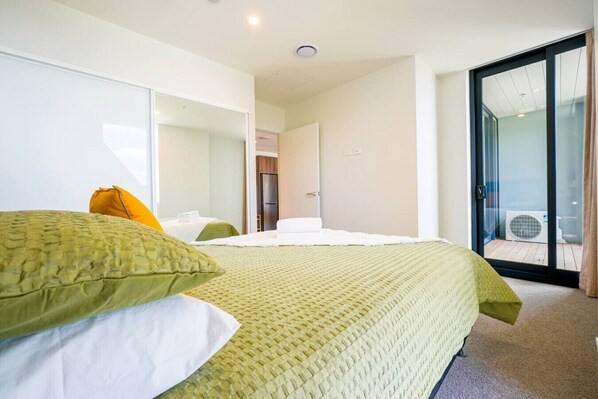 A hotel room with a bed, a chair, a door, and a view of the outside.