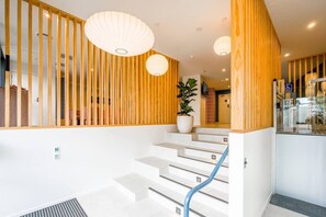 A modern hotel interior with a staircase, wooden paneling, and pendant lighting.