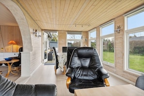 A modern interior with a wooden ceiling, large windows, a dining area, and a leather chair.