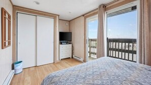 A bedroom with a bed, a television on a dresser, a sliding glass door to a balcony, and a white door. - Charming 1-bedroom condo in tranquil Dennis with AC (Dennis)