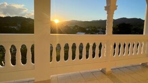 A balcony with a view of the sunset over a mountainous landscape.