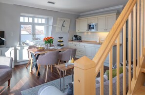 Une cuisine moderne avec des meubles blancs, un four à micro-ondes en acier inoxydable et un escalier en bois.