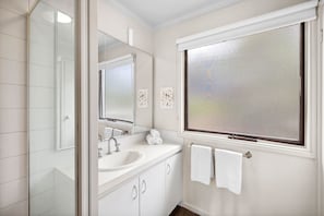 A bathroom with a white sink, mirror, and window. - Fairhaven Escape (Fairhaven)