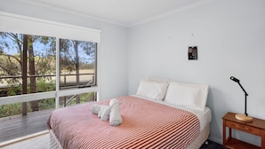 A bedroom with a large window, a bed with striped bedding, a bedside table with a lamp, and a small wall decoration. - Fairhaven Escape (Fairhaven)