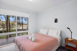 A bedroom with a large window, a bed with striped bedding, a bedside table with a lamp, and a small wall decoration. - Fairhaven Escape (Fairhaven)