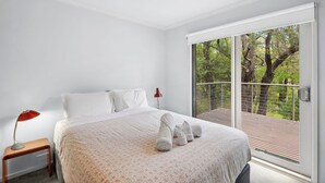 Una camera da letto con un letto, un comodino, una lampada e vista su un balcone alberato.