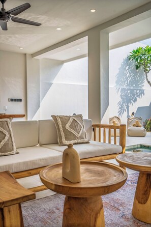 Un área de estar moderna con un sofá, mesas de madera y un ventilador de techo.