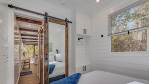 Une chambre avec un grand lit, une porte coulissante et une fenêtre donnant sur les arbres.