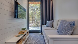 Un salon moderne avec un canapé, une table basse et une vue sur une forêt, visible à travers une grande fenêtre.