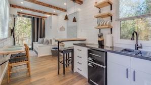 Une cuisine moderne avec des meubles blancs, un réfrigérateur noir et des éléments décoratifs en bois au plafond et sur les étagères.