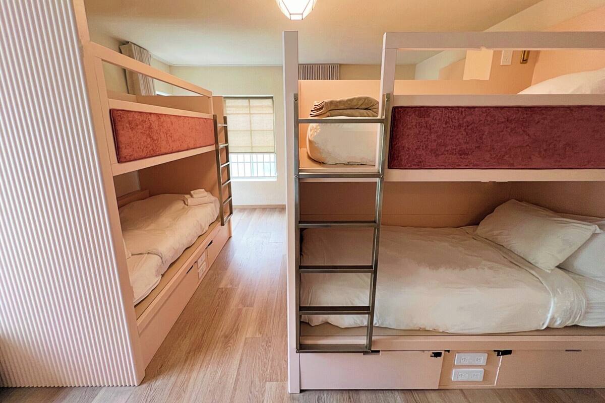 A bunk bed room with a wooden floor, a window with blinds, and a wall-mounted light fixture.