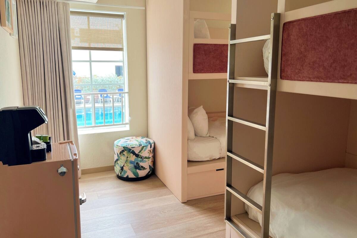 A bedroom with bunk beds, a small round table, a window with curtains, and a view of a pool outside.
