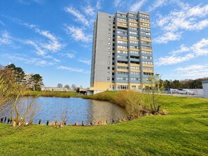 A multi-story residential building with a flat roof, a small pond, and a grassy area in the foreground. - SHH3 - Stunning Vacation Rental with Ocean View, Pool, and Sauna - House (Cuxhaven)