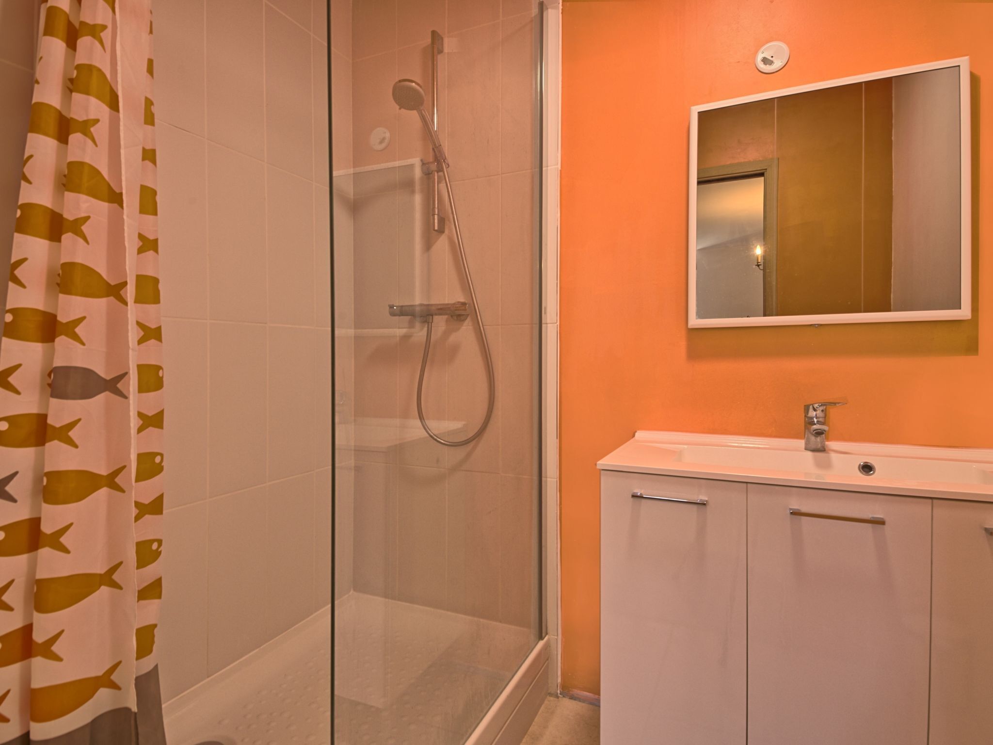 Een badkamer met een glazen douchecabine, een witte wastafel en een oranje wand.