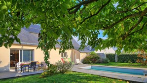 A backyard with a swimming pool, a dining area, and a house with a sloped roof. - Villa au Parc Ny by Interhome (Pénestin)