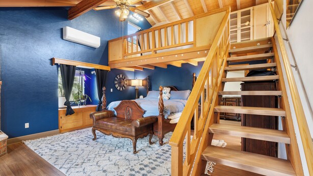 Een kamer met een hoogslaper, een houten trap, een houten bureau en een groot raam.