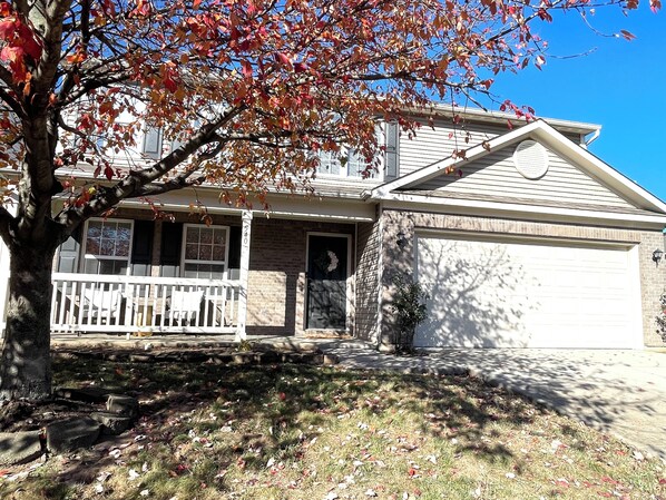 A two-story house with a front porch, a garage, and a tree with autumn leaves.