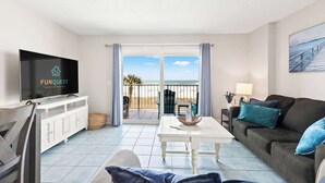 A living room with a television, a white table, a sofa, and a balcony with a view of the beach. - The Summit 301 (Panama City Beach)