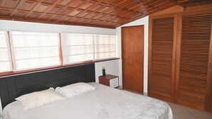 A bedroom with a bed, a nightstand, a wooden wardrobe, and a window with blinds.