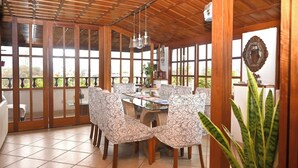 A dining area with a wooden ceiling, patterned chairs, a glass table, and large windows.