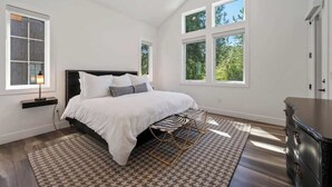 A bedroom with a large bed, a nightstand, a dresser, and two windows. - Idaho Club Golf Course | Luxe Living & Hot Tub (Sandpoint)