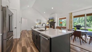A modern kitchen with a large island, built-in appliances, and a dining area with a view of the outdoors. - Idaho Club Golf Course | Luxe Living & Hot Tub (Sandpoint)
