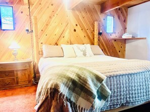 A wooden-paneled bedroom with a bed, pillows, a nightstand, and a wall-mounted shelf.