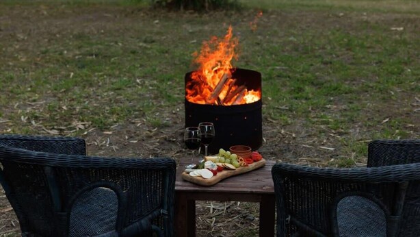 A fire pit with a wooden table and two wicker chairs in a grassy outdoor area.