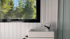 A bathroom with a white sink, a faucet, and a window with a view of trees.