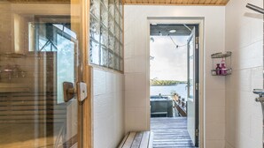 Un baño con cabina de ducha de vidrio, un banco de madera, vista a un lago y un estante pequeño con artículos de aseo.