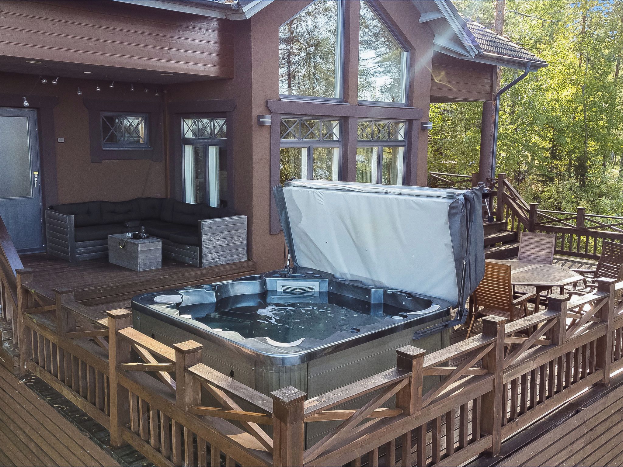 Une terrasse en bois avec un jacuzzi, du mobilier d’extérieur et un espace salon abrité.