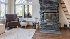 Un salón acogedor con chimenea de piedra, un sillón cómodo y un ventanal con vistas al exterior.