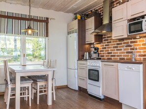 Una cocina con pared de ladrillo, armarios blancos, campana extractora de acero inoxidable y microondas empotrado, además de un comedor con mesa y sillas.