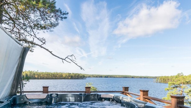 Jacuzzi con muelle de madera y vista a un lago y bosque.