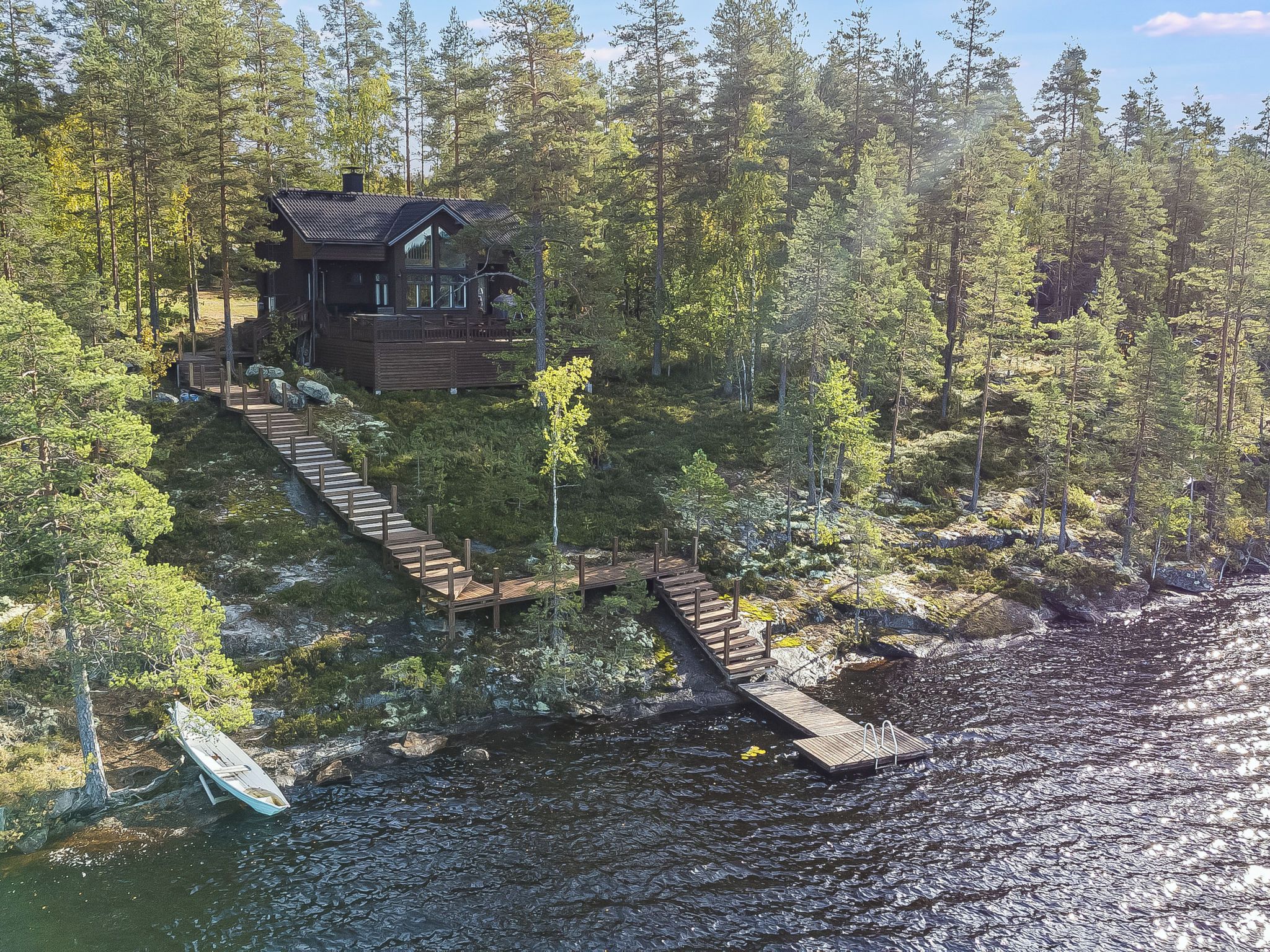 A cabin with a wooden deck leading to a dock over water, surrounded by dense forest.