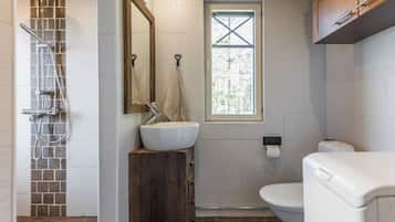 Ein Badezimmer mit einer Steindusche, einem Holzbidet, einem weißen Waschbecken, einer Toilette und einem Fenster mit Blick auf Bäume.