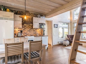 A modern kitchen with a brick wall, wooden cabinets, and a dining area with a wooden table and chairs. - Nuottarinne by Interhome (Keuruu)