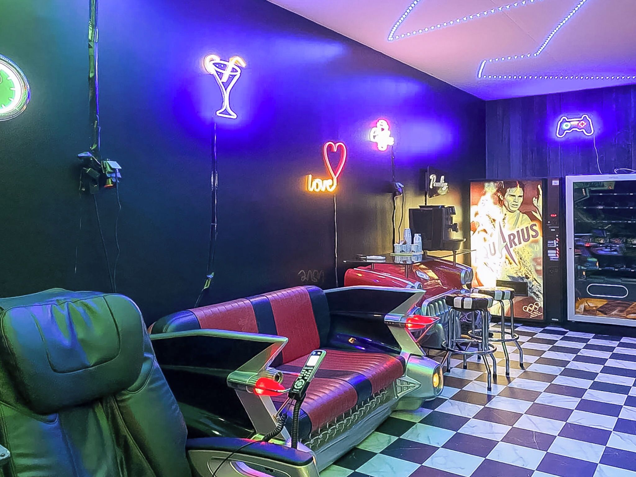 A room with a checkered floor, a neon-lit wall, a sofa, a gaming console, and a poster of a sports figure.