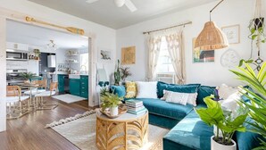 Un salon moderne avec un canapé de couleur turquoise, une table basse ronde en osier et un coin repas comprenant une table et des chaises blanches.